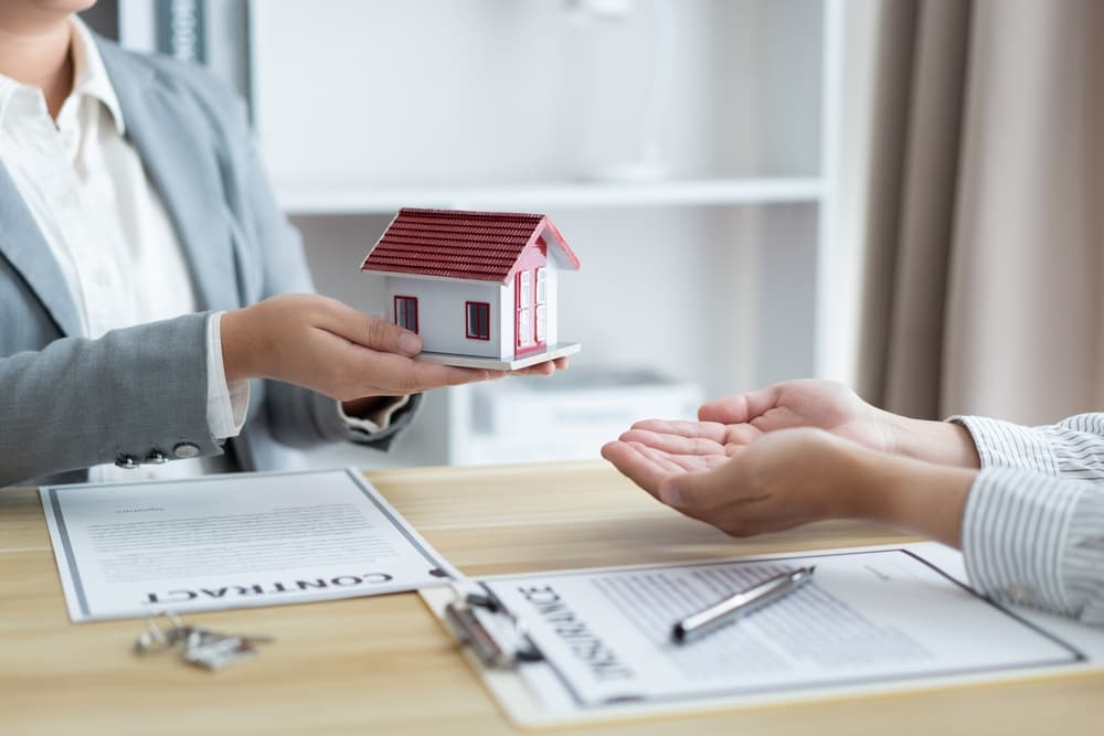 The insurance agent is holding a model house and presenting it to his client.
