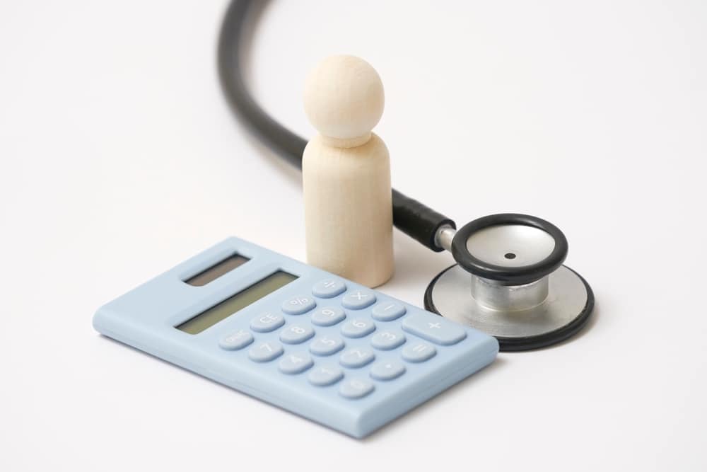 the medical expenses image, the wooden doll, stethoscope and a calculator in white background
