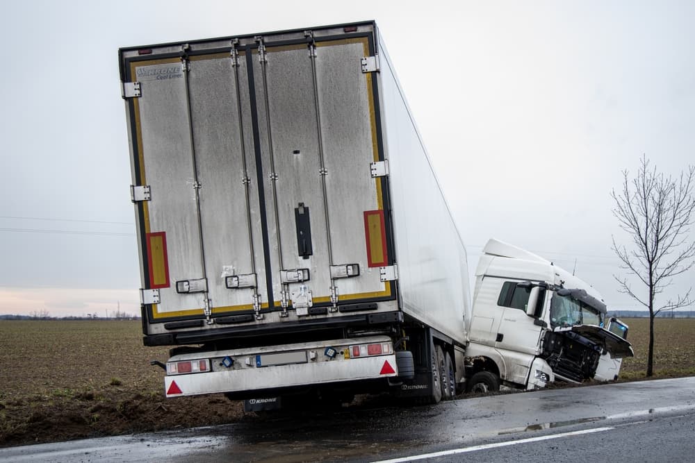 A large truck crashed into a ditch off the road, with significant damage to the cab.