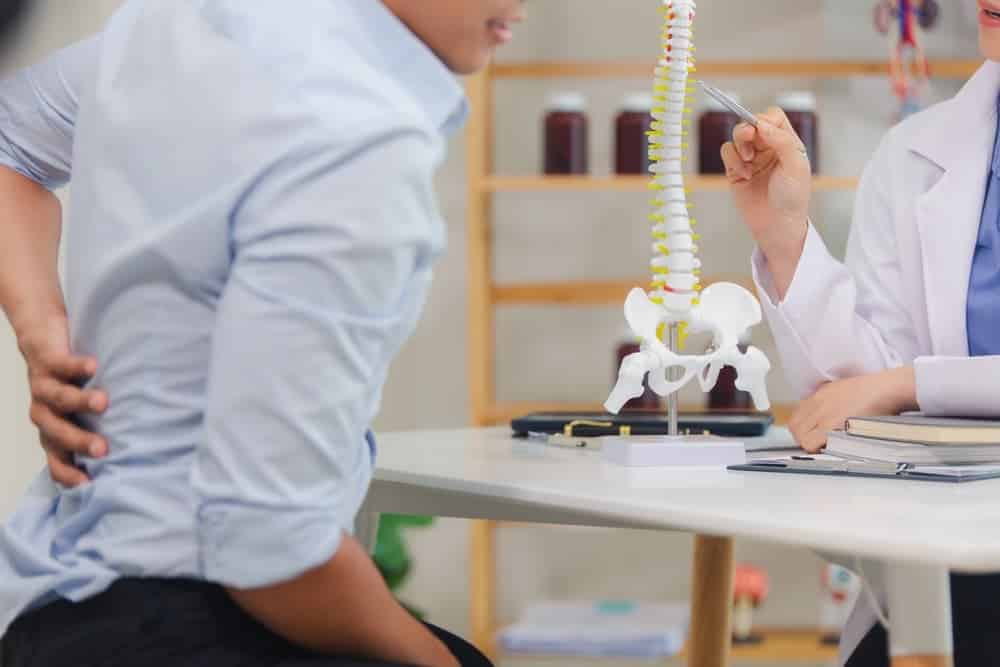 Un paciente con lesión de la médula espinal consulta a un médico, quien le explica los problemas de la columna utilizando un modelo de columna.