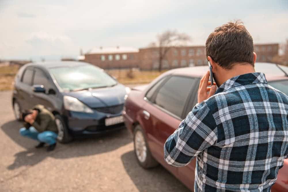 Man calling for help after a car accident, while another person appears distressed.
