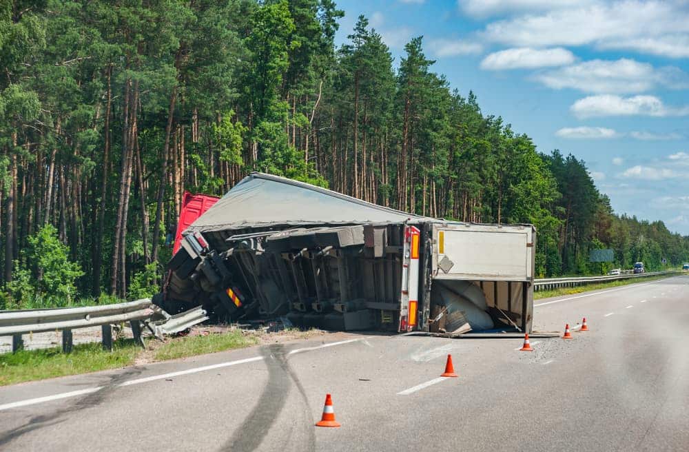 Rollover semi-truck on a highway with scattered cargo and traffic cones nearby.
