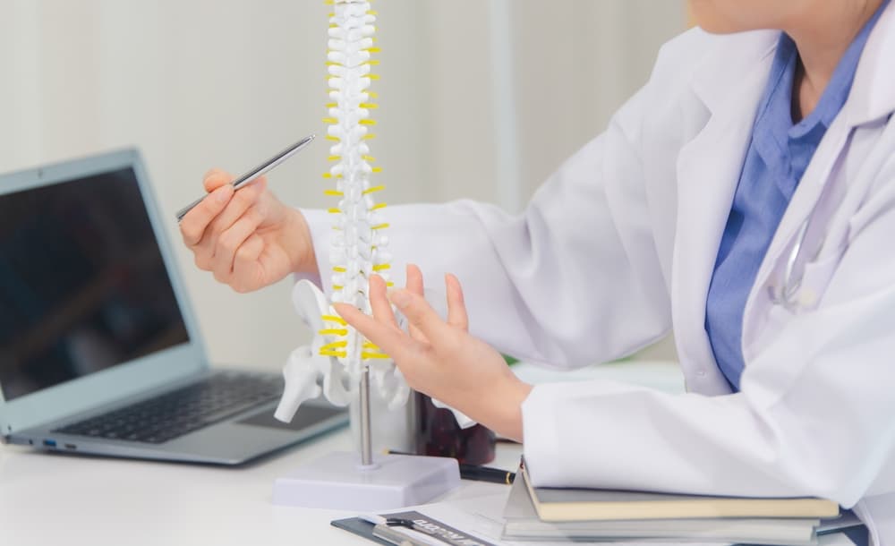 Un médico ortopedista explica un modelo de columna a un paciente y habla sobre el dolor de espalda y los trastornos de la columna.