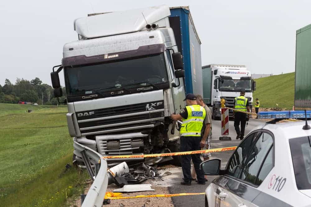 Damaged truck crashed into guardrail with police officers inspecting the accident scene.