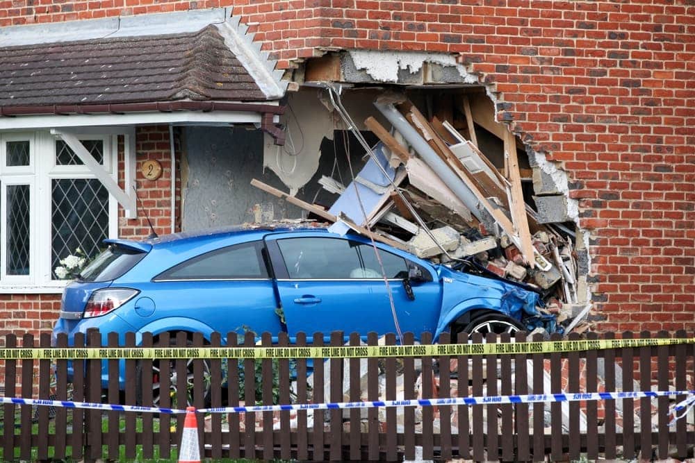 A blue car crashes into a brick house, highlighting questions about fault and filing a claim.
