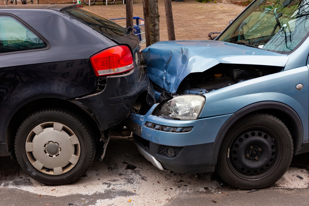 Front end of a blue car crashed into the rear bumper of a dark-colored vehicle in a rear-end collision