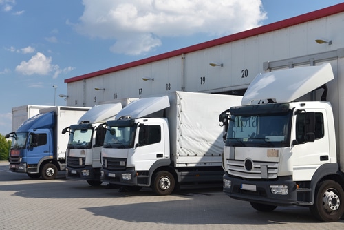 Row of cargo trucks parked at loading docks outside a warehouse.