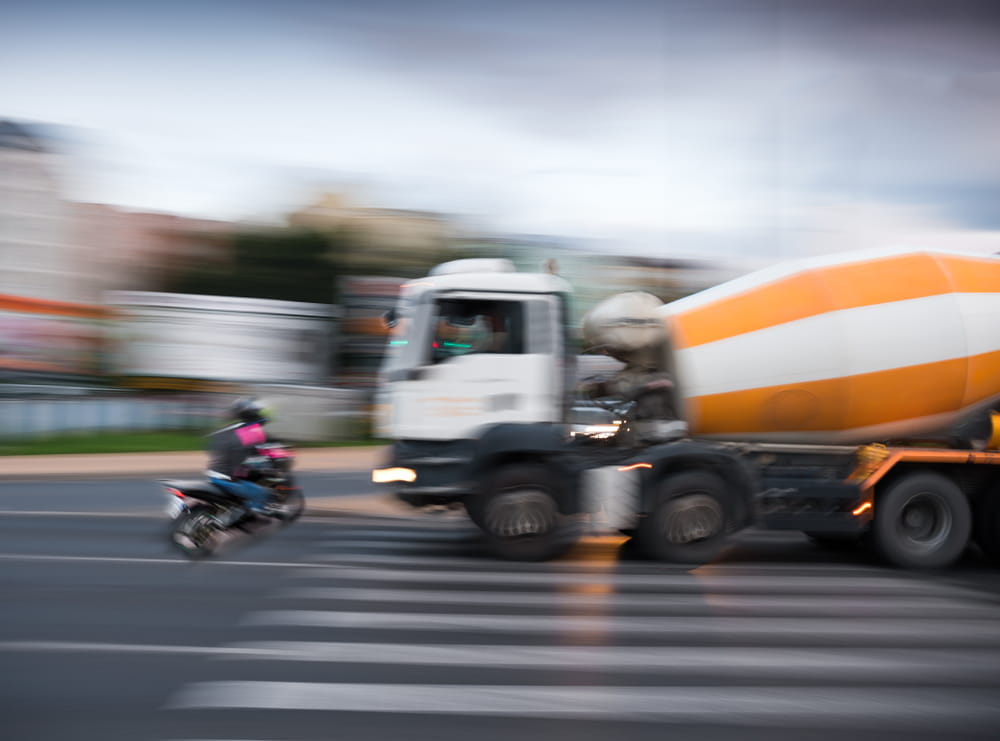 Large cement truck passing motorcycle at crosswalk illustrating visibility and traffic dangers for riders