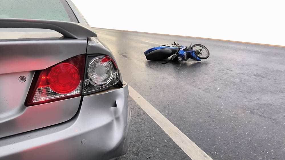 Vehicle and motorcycle collision scene on wet roadway illustrating dangerous suburban traffic conditions