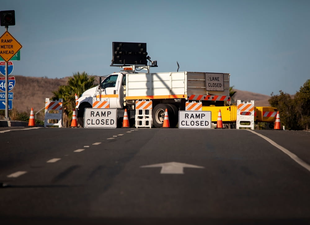 Commercial work truck blocking freeway ramp with traffic cones and lane closure signs in California