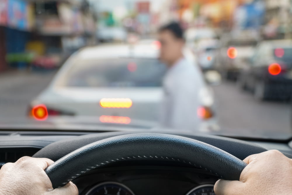 Driver&rsquo;s perspective approaching a pedestrian in heavy urban traffic near a transit center