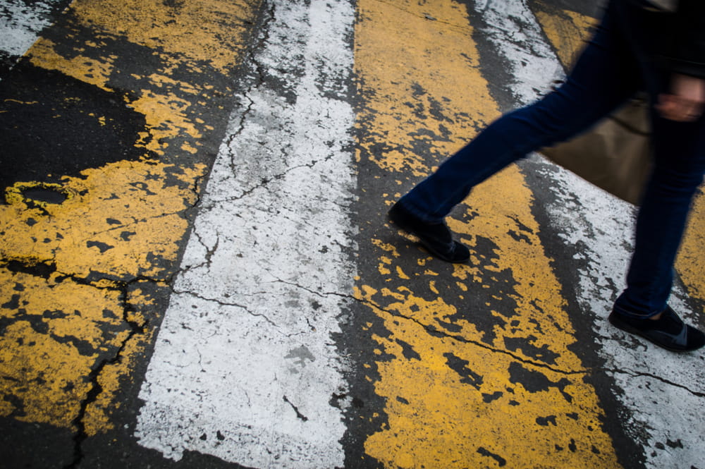 Pedestrian walking across a worn crosswalk near a busy transit area