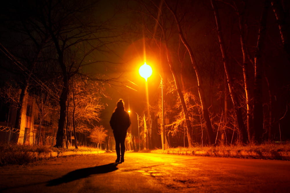 Pedestrian walking along a dark road at night under street lighting